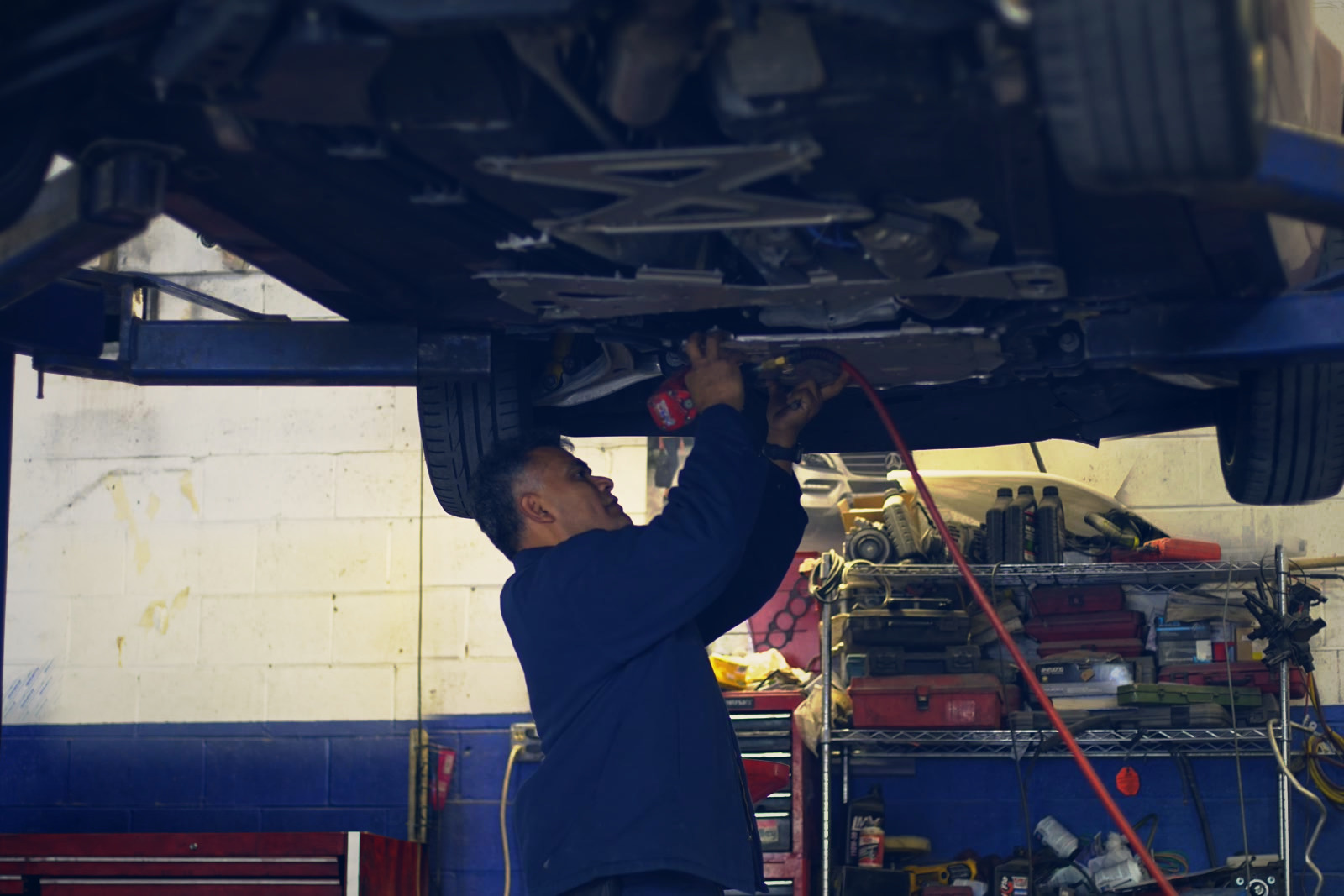 A technician using an impact gun under a car on the lift